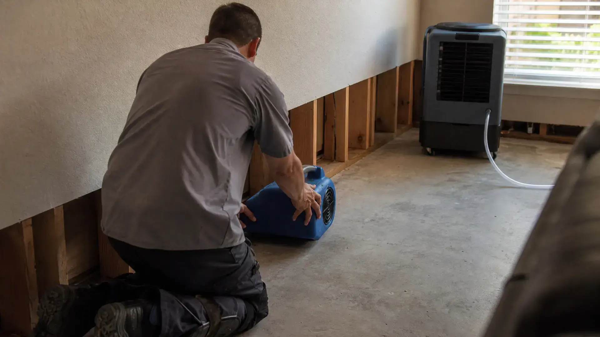 A restoration technician setting an air mover against a flood-cut wall in a San Marcos living room