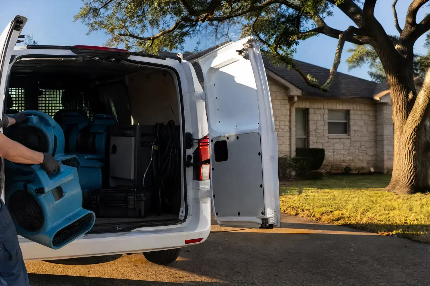 Restoration equipment being unloaded from a work van outside a San Marcos home