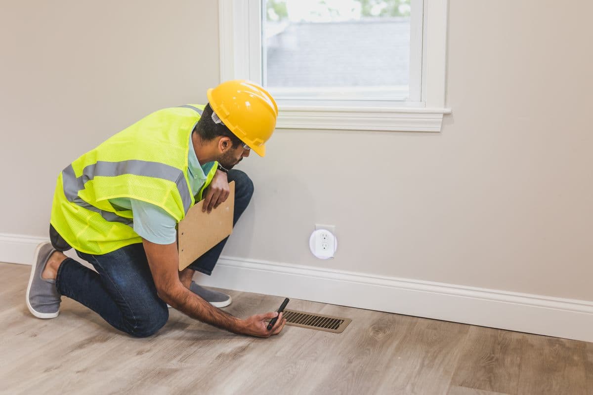 A technician scanning an interior wall with a thermal imaging camera, reading points marked in tape