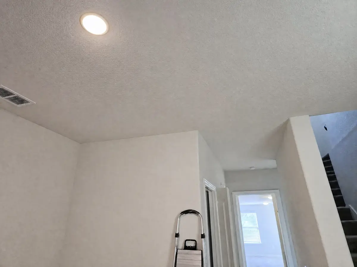 The same ceiling repaired with new drywall textured to match and painted clean white, flat and uniform with no stain or bulge.