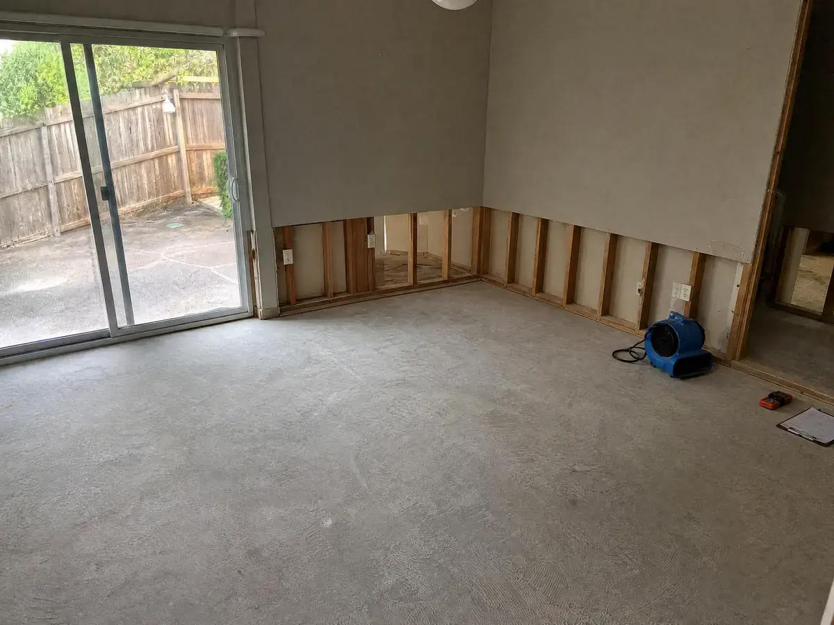 The same living room on day four, slab uniformly dry, framing light in tone and the drying equipment being removed.