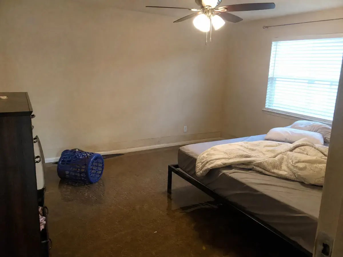 Bedroom with about two inches of standing water across soaked carpet, a water line on the lower drywall and a warped baseboard.